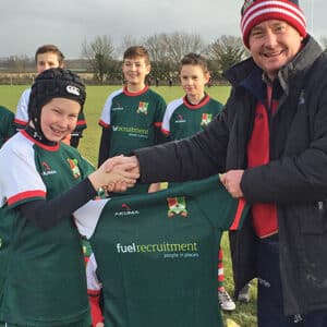 Murray West shaking hands with young rugby player holding up rugby shirt with Fuel Recruitment sponsorship logo on